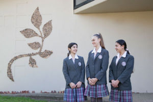 Three students in front of Mary MacKillop Catholic College Wakeley school emblem